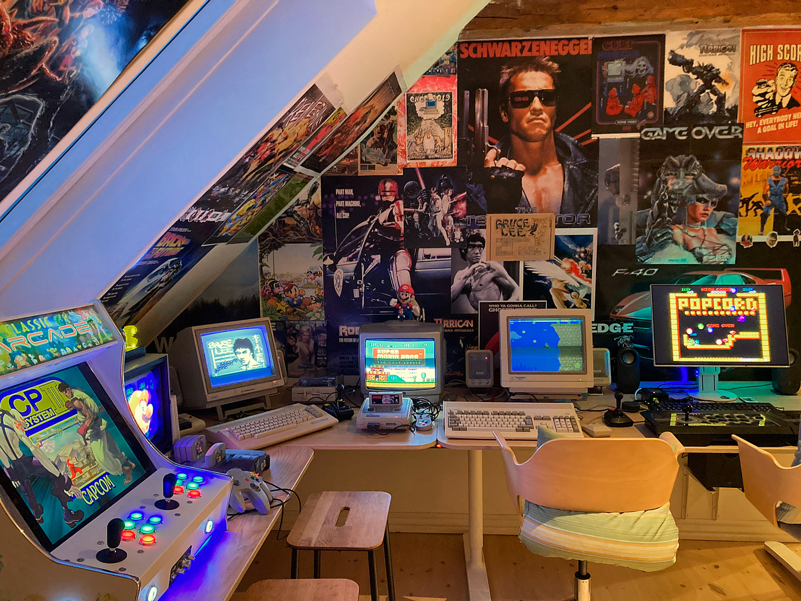 A cozy retro gaming setup with multiple machines and 80s posters